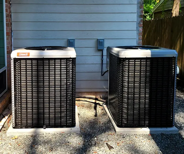 Two condensers set on fresh pads alongside a house