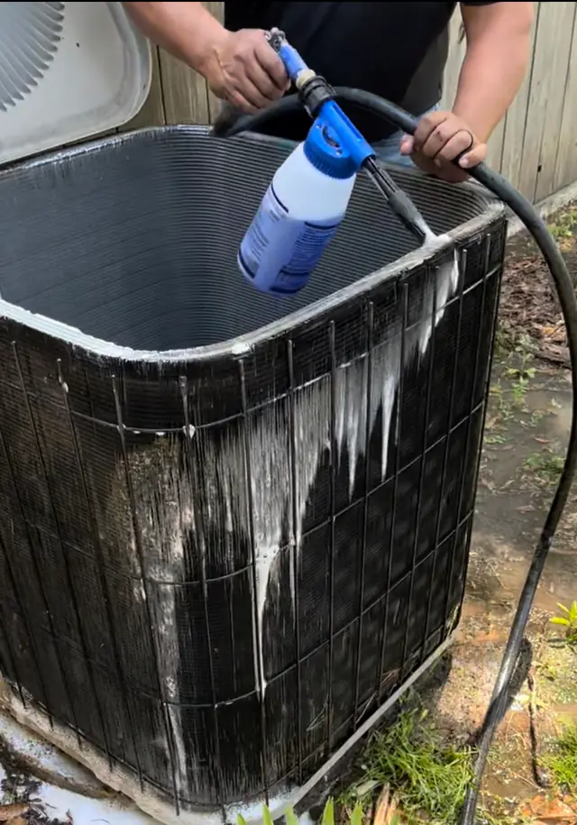 Technician washing a condenser coil with a hose attachment